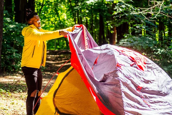 Afro-americano em amarelo jacker colocando em uma barraca na floresta — Fotografia de Stock