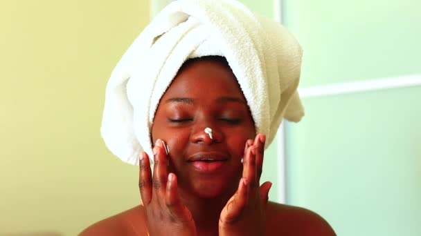 Mulher hispânica com toalha na cabeça aplicando creme no rosto em casa — Vídeo de Stock