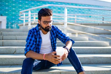 Kakao bardaklı Arap adam dışarıda merdivenlerde oturuyor.