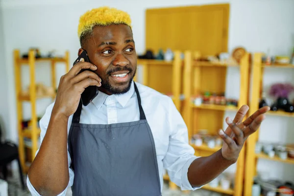 Afro mužský hrnčíř mluví do telefonu ve svém studiu — Stock fotografie