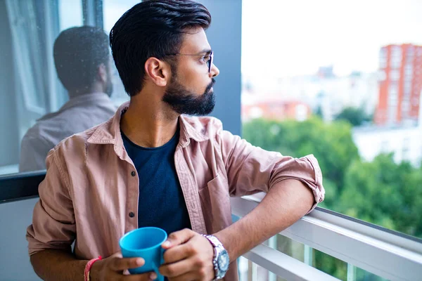 Homem árabe em vestido casual holning uma xícara azul e olhando sonhadamente — Fotografia de Stock