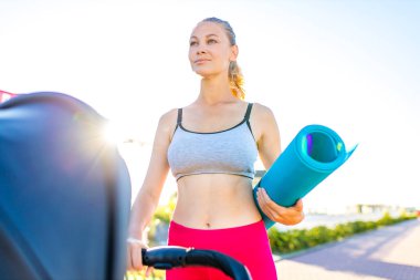 Sarışın genç anne dışarıda çalışıyor. Tropik plajda yoga minderiyle ısınıyor.