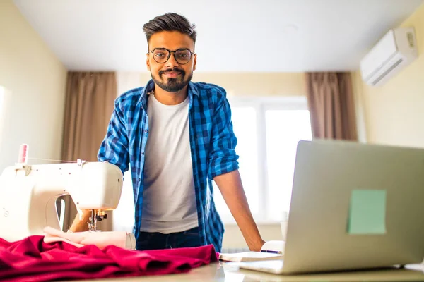 Indischer Schneider asiatischer Mann Designer näht Kleidung auf Nähmaschine neben Laptop Wohnung Arbeitsplatz — Stockfoto