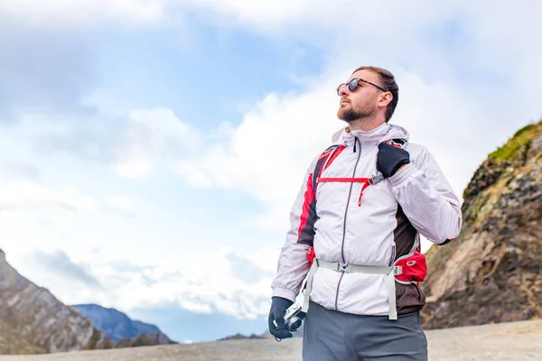 Giovane uomo barbuto indossa giacca bianca soffio in piedi vicino a una montagna — Foto Stock