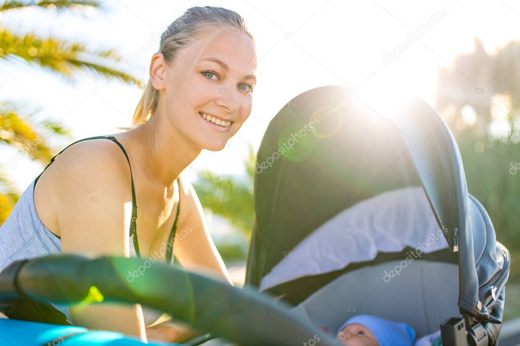 happy blonde woman kissind and feelinf adore to her stroll new born kid in tropics beach park outdoors