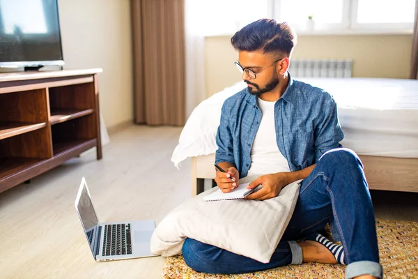 Indiana barbuda masculino sentado no chão e fazendo cálculos financeiros negócios on-line em novo apartamento — Fotografia de Stock