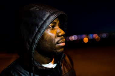 Kapüşonlu İspanyol adam parktaki alacakaranlık sokaklarına bakıyor.