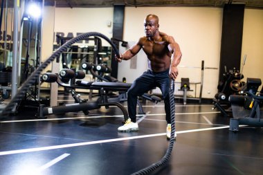 Genç Afrikalı kas sporcusu spor salonunda halatlarla çalışıyor.