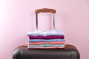 Renkli mükemmel katlanmış giyim üzerine plastik bavul bagaj yığını. Farklı pastel renk gömlek ve Kazaklar soluk pembe duvar zemin üzerine yığını. Yakın çekim, görünümü, kopya alanı top.