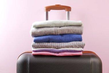 Renkli mükemmel katlanmış giyim üzerine plastik bavul bagaj yığını. Farklı pastel renk gömlek ve Kazaklar soluk pembe duvar zemin üzerine yığını. Yakın çekim, görünümü, kopya alanı top.