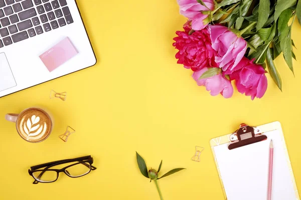 Feminine desktop, close up of laptop keyboard, blank clipboard, coffee, peony flowers, eyewear. Flat lay composition, notebook computer, cappuccino cup, glasses eye wear, white background. Copy space.