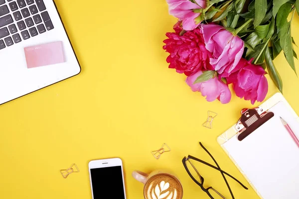 Feminine desktop, close up of laptop keyboard, blank clipboard, coffee, peony flowers, eyewear. Flat lay composition, notebook computer, cappuccino cup, glasses eye wear, white background. Copy space.