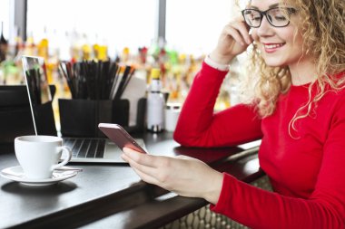 Yeni iletiler için trendy onun smartphone kontrol genç çekici kadın. Arka plan üzerinde büyük camları olan hipster kahve evinde ahşap masa şık dizüstü bilgisayarda çalışan kadın serbest meslek.