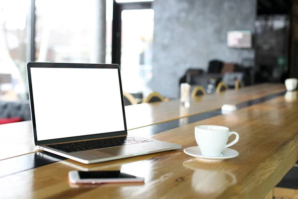 Boş ekran dizüstü bilgisayar ve cep telefonu ile kahve hipster cafe bar, büyük pencereler ahşap masa üzerinde. Smartphone becerikli alet ve dizüstü bilgisayar. Serbest çalışma kavramı. Yakın çekim, uzay, arka plan kopya.
