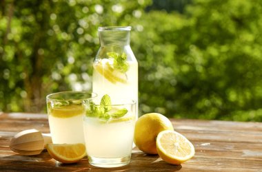 Limonata sürahi, meyva suyu sıkacağı, iki bardak limon dilimleri ve nane yaprakları kahverengi grunged ahşap masa, ülke tarafı yeşillik arka plan ile buz soğuk ferahlatıcı narenciye içecek dolu. Yakın çekim, alanı Kopyala.
