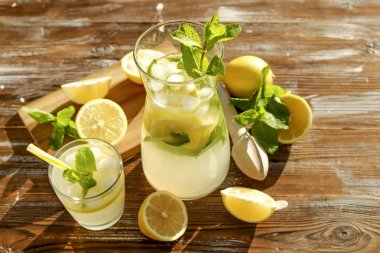 Buzlu limonata sürahi, ahşap meyve sıkacağı ve limon dilimleri, nane yaprakları ve kahverengi grunged Ahşap dokulu masa güneşli, arka plan sarı saman ile soğuk narenciye içecek bir bardak. Yakın çekim, alanı Kopyala.