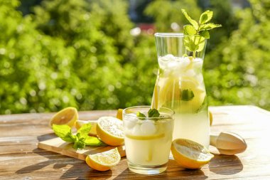 Buzlu limonata sürahi, meyve sıkacağı ve limon dilimleri, nane yaprakları ve kahverengi grunged ahşap masa, ülke tarafı yeşillik arka plan üzerinde sarı payet ile soğuk narenciye içecek bir bardak. Yakın çekim, alanı Kopyala.