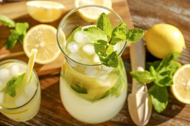 Buzlu limonata sürahi, ahşap meyve sıkacağı ve limon dilimleri, nane yaprakları ve kahverengi grunged Ahşap dokulu masa güneşli, arka plan sarı saman ile soğuk narenciye içecek bir bardak. Yakın çekim, alanı Kopyala.