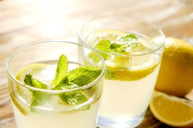 İki bardak nane ile buz soğuk ferahlatıcı limonata içecek tam güneş ışığı altında kahverengi grunged ahşap masa üzerinde olgun organik limon, bütün ve yarıya dilim bırakır. Arka plan, kopya alanı, yakın çekim.