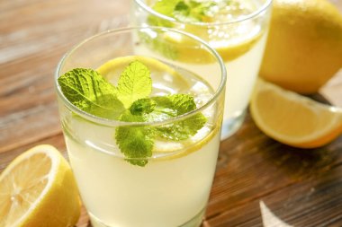 İki bardak nane ile buz soğuk ferahlatıcı limonata içecek tam güneş ışığı altında kahverengi grunged ahşap masa üzerinde olgun organik limon, bütün ve yarıya dilim bırakır. Arka plan, kopya alanı, yakın çekim.