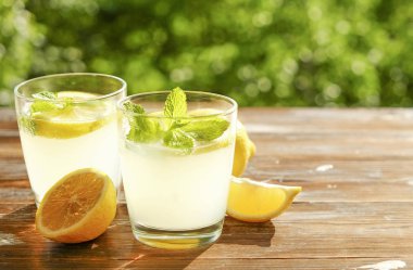 İki bardak buz soğuk ferahlatıcı limonata içecek nane w / dolu kahverengi grunged ahşap masa üzerinde olgun organik limon, ülke tarafı yeşillik arka plan dilim güneş ışığı altında bırakır. Uzay kopyalayın, yakın çekim.