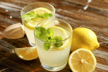 İki bardak buz dolu ferahlatıcı soğuk limonata İçecek taze nane w / güneş ışığında yaprakları kahverengi grunged ahşap masa, meyva suyu sıkacağı, olgun organik limon, bütün ve dilimlenmiş. Arka plan, kopya alanı, yakın çekim.