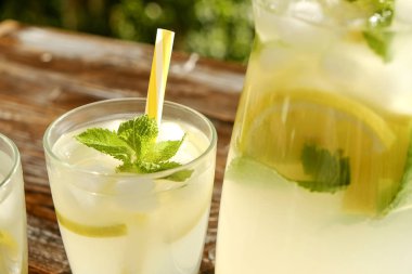 Limonata sürahi ve iki bardak soğuk buz, limon dilimleri, nane yaprakları ve kahverengi grunged ahşap masa, ülke tarafı yeşillik arka plan üzerinde payet ile narenciye içecek yenileniyor. Yakın çekim, alanı Kopyala.