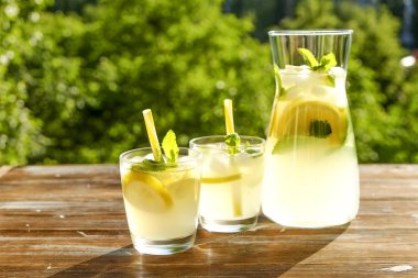 Limonata sürahi ve iki bardak soğuk buz, limon dilimleri, nane yaprakları ve kahverengi grunged ahşap masa, ülke tarafı yeşillik arka plan üzerinde payet ile narenciye içecek yenileniyor. Yakın çekim, alanı Kopyala.