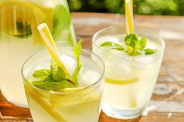 Limonata sürahi ve iki bardak soğuk buz, limon dilimleri, nane yaprakları ve kahverengi grunged ahşap masa, ülke tarafı yeşillik arka plan üzerinde payet ile narenciye içecek yenileniyor. Yakın çekim, alanı Kopyala.