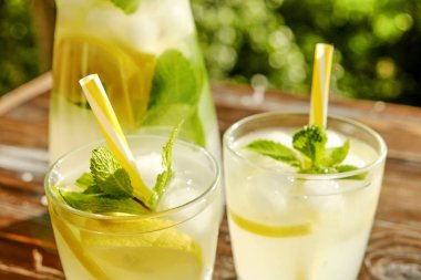 Limonata sürahi ve iki bardak soğuk buz, limon dilimleri, nane yaprakları ve kahverengi grunged ahşap masa, ülke tarafı yeşillik arka plan üzerinde payet ile narenciye içecek yenileniyor. Yakın çekim, alanı Kopyala.