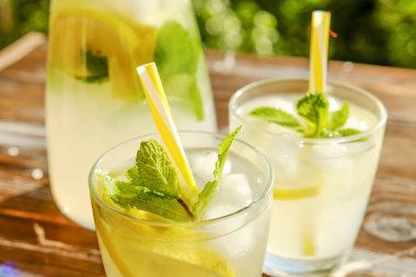 Limonata sürahi ve iki bardak soğuk buz, limon dilimleri, nane yaprakları ve kahverengi grunged ahşap masa, ülke tarafı yeşillik arka plan üzerinde payet ile narenciye içecek yenileniyor. Yakın çekim, alanı Kopyala.