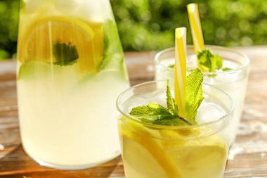 Limonata sürahi ve iki bardak soğuk buz, limon dilimleri, nane yaprakları ve kahverengi grunged ahşap masa, ülke tarafı yeşillik arka plan üzerinde payet ile narenciye içecek yenileniyor. Yakın çekim, alanı Kopyala.