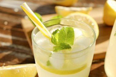 Buzlu limonata sürahi, ahşap meyve sıkacağı ve limon dilimleri, nane yaprakları ve kahverengi grunged Ahşap dokulu masa güneşli, arka plan sarı saman ile soğuk narenciye içecek bir bardak. Yakın çekim, alanı Kopyala.