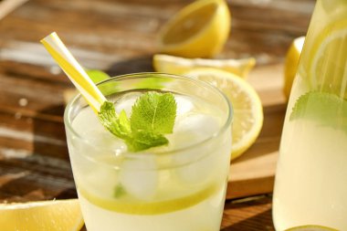 Buzlu limonata sürahi, ahşap meyve sıkacağı ve limon dilimleri, nane yaprakları ve kahverengi grunged Ahşap dokulu masa güneşli, arka plan sarı saman ile soğuk narenciye içecek bir bardak. Yakın çekim, alanı Kopyala.