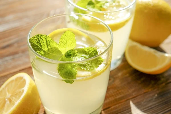 İki bardak nane ile buz soğuk ferahlatıcı limonata içecek tam güneş ışığı altında kahverengi grunged ahşap masa üzerinde olgun organik limon, bütün ve yarıya dilim bırakır. Arka plan, kopya alanı, yakın çekim.