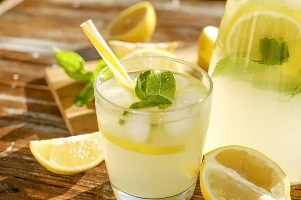 Buzlu limonata sürahi, ahşap meyve sıkacağı ve limon dilimleri, nane yaprakları ve kahverengi grunged Ahşap dokulu masa güneşli, arka plan sarı saman ile soğuk narenciye içecek bir bardak. Yakın çekim, alanı Kopyala.