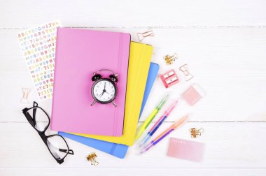 Okul malzemeleri, sarı ve mavi defter, pembe kalemtıraş, gözüne gözlük, renkli kalem, altın bağlayıcı ve beyaz ahşap masa üzerinde silgi kadınsı kümesi. Arka plan, uzay kopya, ana sayfa görünümü, yat.