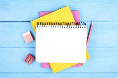 Kadınsı dizi okul malzemeleri, sarı pembe kapak, sayfa boş defter, kalemtıraş, renkli kalem, bağlayıcılar, çıkartmalar ve silgi, mavi ahşap masa açın. Arka plan, uzay kopya, ana sayfa görünümü, yat