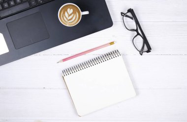 Dizüstü bilgisayar klavye ve touchpad, fincan cappuccino kahve, boş defter cheet, gözlük ve kalem Beyaz ahşap masa arka plan dokulu. Çalışma alanı minimalizm, düz yatıyordu, en iyi görünüm, kopya alanı