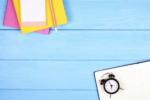 Feminine workspace, to do list, pink & yellow cover, open notebook, blank pages, mini alarm clock on blue wooden table background. Back to school concept. Girls desk w/ supplies. flat lay, copy space.