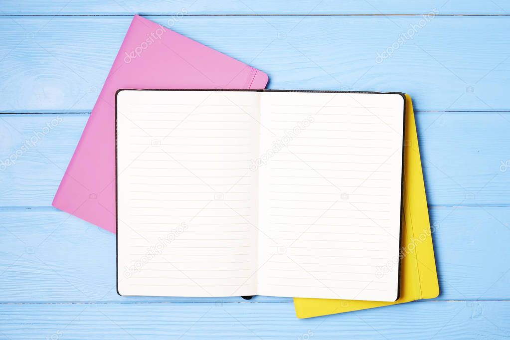 Top view of notepad, pink and yellow notebook cover and pen on a blue wooden desk background with blank paper sheet and checkbox for copy space text. To do list concept. Close up, minimal flat lay.