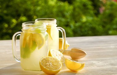 İki mason kavanoza ev yapımı limonata, organik olgun limon, bütün ve yarıya, nane, Beyaz ahşap masa, ülke yan ağaç bitki örtüsü arka plan üzerinde meyve sıkacağı dilimleri bardak. Yakın çekim, görünümü, kopya alanı top.