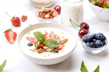Yayınlama seçeneğini granola kase fındık, tahıl, meyve ve çilek, Yunan yoğurt karışımı ile. Sağlıklı vejetaryen kahvaltı, organik çilek, yaban mersini, nane, badem. Yakın çekim, görünümü, arka plan top.