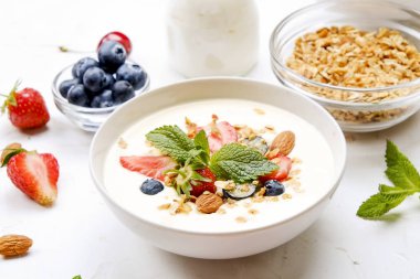 Yayınlama seçeneğini granola kase fındık, tahıl, meyve ve çilek, Yunan yoğurt karışımı ile. Sağlıklı vejetaryen kahvaltı, organik çilek, yaban mersini, nane, badem. Yakın çekim, görünümü, arka plan top.