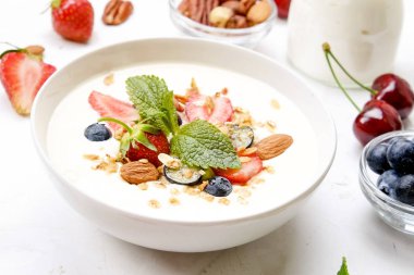 Yayınlama seçeneğini granola kase fındık, tahıl, meyve ve çilek, Yunan yoğurt karışımı ile. Sağlıklı vejetaryen kahvaltı, organik çilek, yaban mersini, nane, badem. Yakın çekim, görünümü, arka plan top.