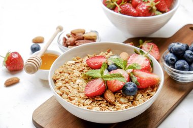 Yayınlama seçeneğini granola kase fındık, tahıl, meyve ve çilek, Yunan yoğurt karışımı ile. Sağlıklı vejetaryen kahvaltı, organik çilek, yaban mersini, nane, badem. Yakın çekim, görünümü, arka plan top.