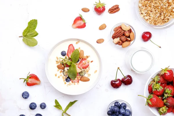 Serving option of granola bowl with mix of nuts, cereals, fruits and berries, greek yogurt. Healthy vegetarian breakfast, organic strawberry, blueberry, mint, almond. Close up, top view, background.