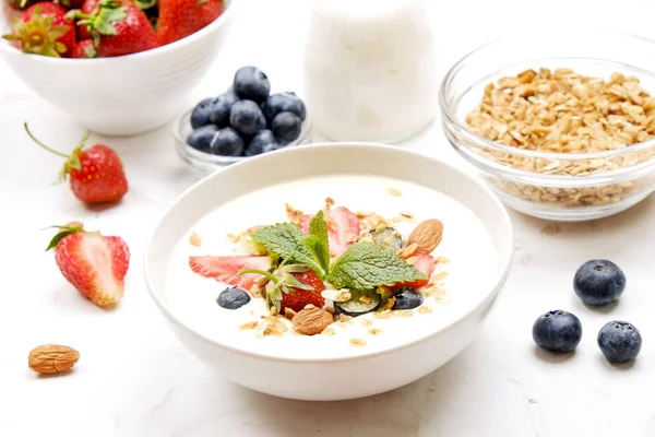 Serving option of granola bowl with mix of nuts, cereals, fruits and berries, greek yogurt. Healthy vegetarian breakfast, organic strawberry, blueberry, mint, almond. Close up, top view, background.