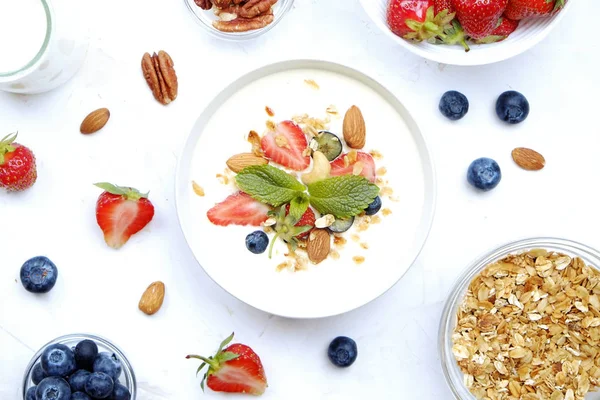 Serving option of granola bowl with mix of nuts, cereals, fruits and berries, greek yogurt. Healthy vegetarian breakfast, organic strawberry, blueberry, mint, almond. Close up, top view, background.