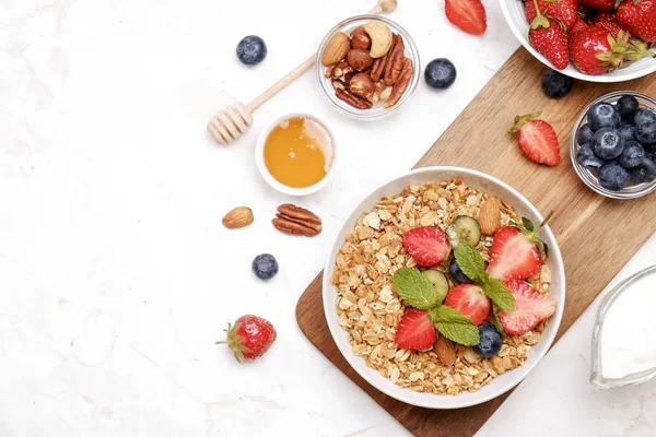 Serving option of granola bowl with mix of nuts, cereals, fruits and berries, greek yogurt. Healthy vegetarian breakfast, organic strawberry, blueberry, mint, almond. Close up, top view, background.